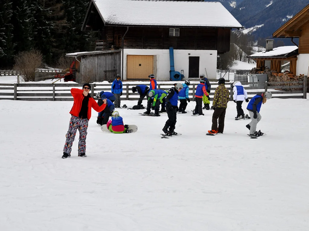 Kinder und Jugendliche üben vor einem Bauernhaus im Schnee.